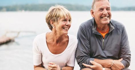 Senior couple sitting on a bench in front of a fire by a lake