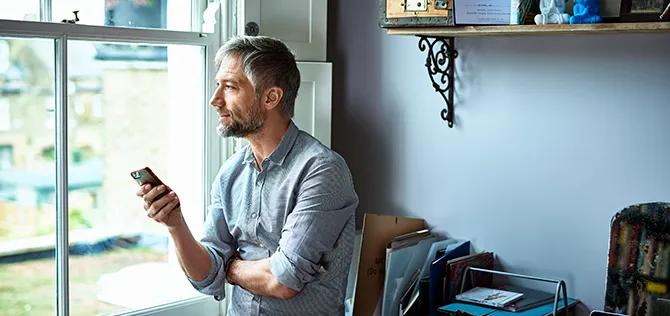Man in his 40s texting on smartphone, sitting on edge of desk and looking away, contemplation, entrepreneur, small business owner, casual businessman