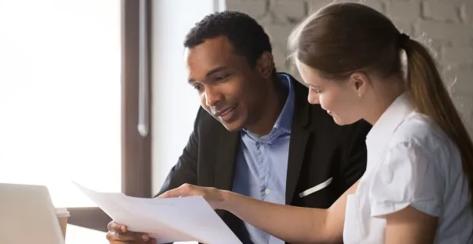 Young male and female colleagues sitting at a desk reviewing benefit paperwork together.