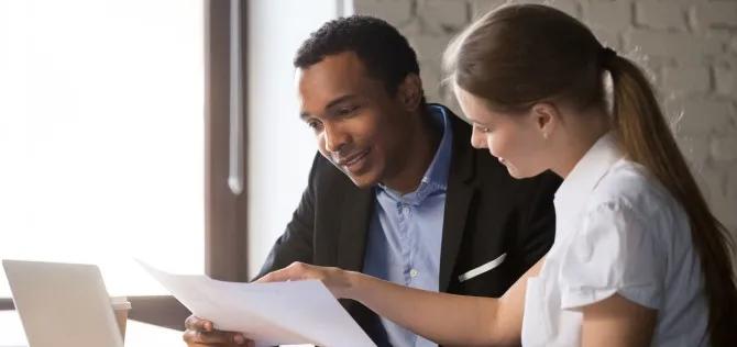 Young male and female colleagues sitting at a desk reviewing benefit paperwork together.