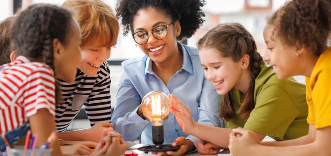 Multiethnic teacher and kids studying electricity and incandescent light bulb at physics lesson in bright classroom