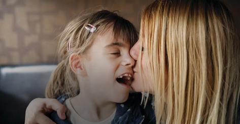 Mother is kissing her daughter that has visual impairment. Genuine emotions, real people.
