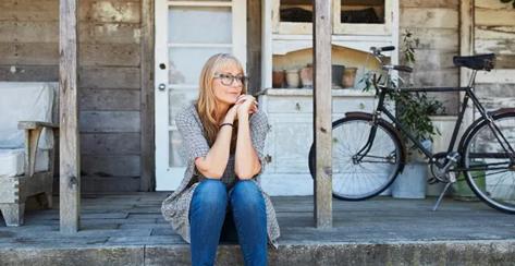 A mid-age woman sitting on a rustic porch.